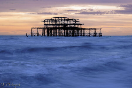 Brighton West Pier bei bewölktem Sonnenuntergang. Im Vordergrund das Meer. Längere Belichtungszeit, deshalb Wellen mehr "fließend "