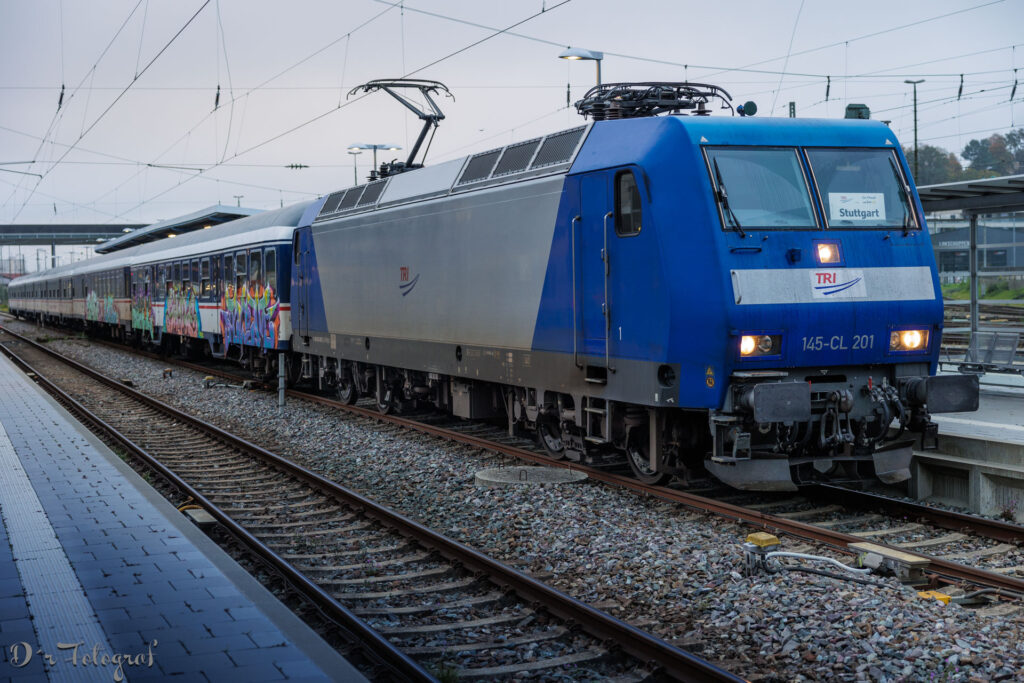 Blaue Elektrolokomotive 145-CL 201 der TRI Train Rental GmbH vor einem Nahverkehrszug. Schräg von vorne aufgenommen