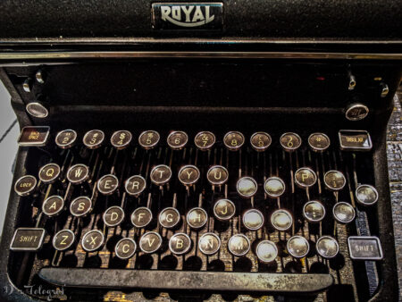Bild zeigt eine alte Schreibmaschine mit unterschiedlich eingedrückten Tasten. Die Schreibmaschine ist Schwarz mit Gold und zeigt das MArkenzeichen "Royal". Es ist nicht die ganze Schreibmaschine zu sehen, sondern nur die Tastatur.
