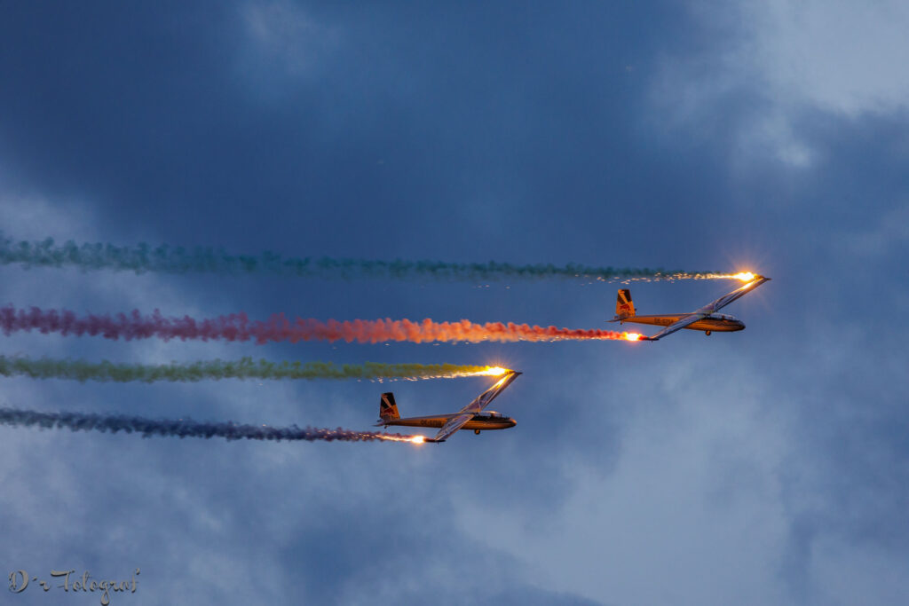 Zwei Segelflugzeuge am Abendhimme im prallelen Formationsflug. Beide Flugzeuge haben farbige Rauchfahnen an den Flügelenden