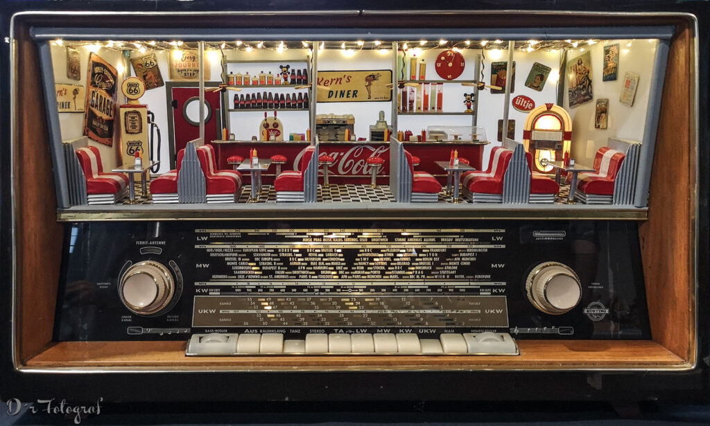 Bild zeigt ein altes Röhrenradio, in welchem statt des Lautsprechers über der Skala ein Miniaturrestaurant im 1950er Jahre US-Stil eingebaut ist