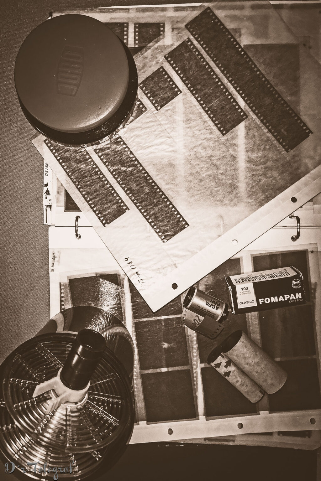 Bild zeigt Utensilien für das Entwickeln von Filmen. Entwicklerdose, Entwicklerspule, zwei Filme und Negativtaschen - Bild ist Monochrom